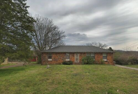 A small brick house with a grey roof and a green lawn in front.
