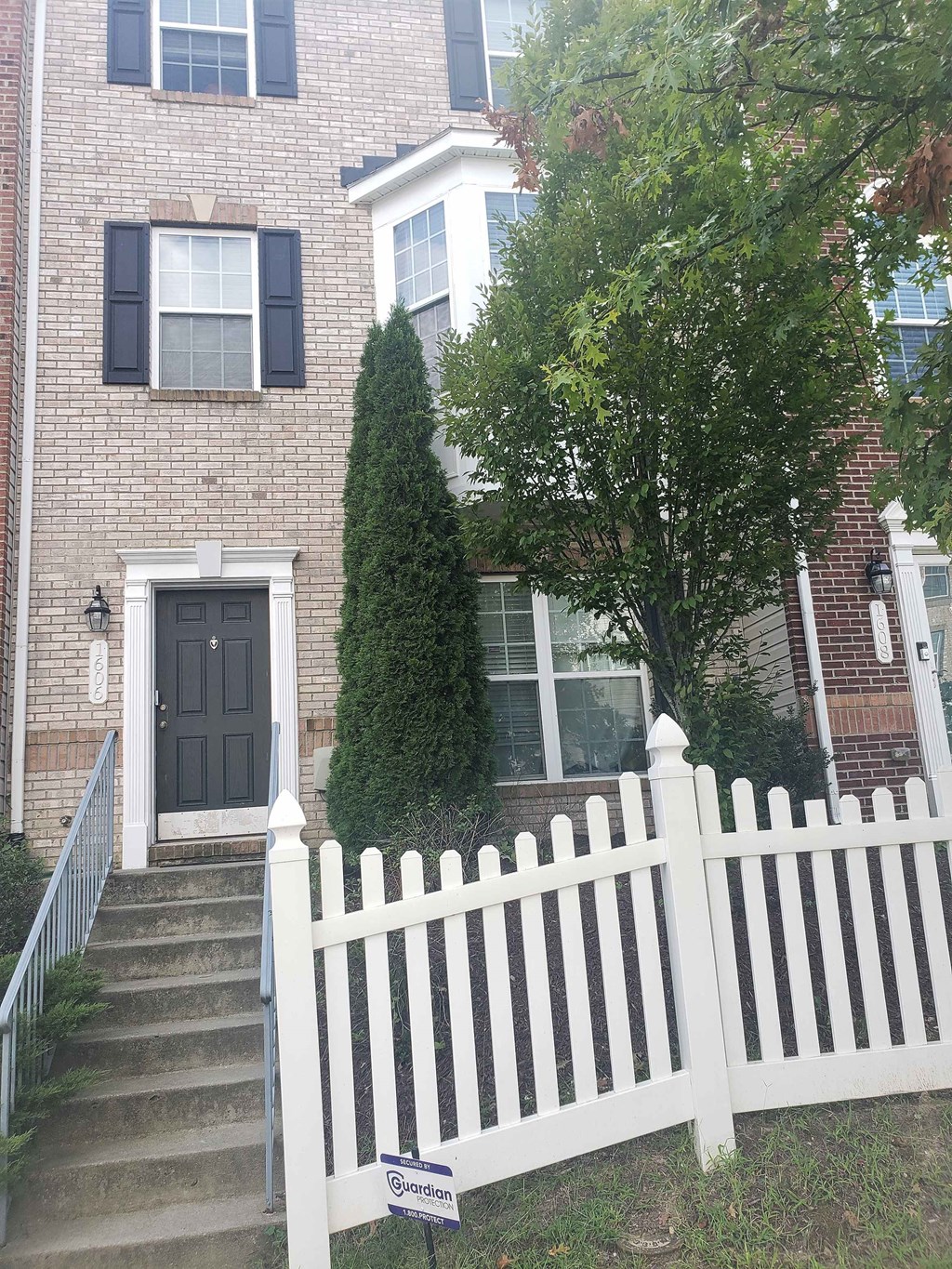 A white picket fence in front of a brick house.
