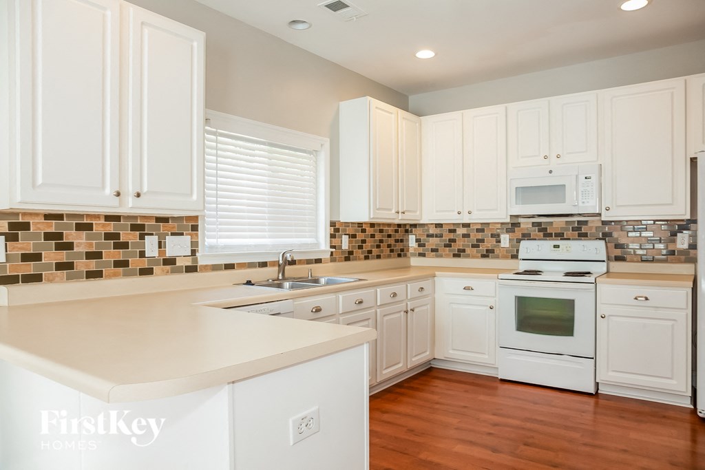 a kitchen with white cabinets and white appliances and a wooden floor