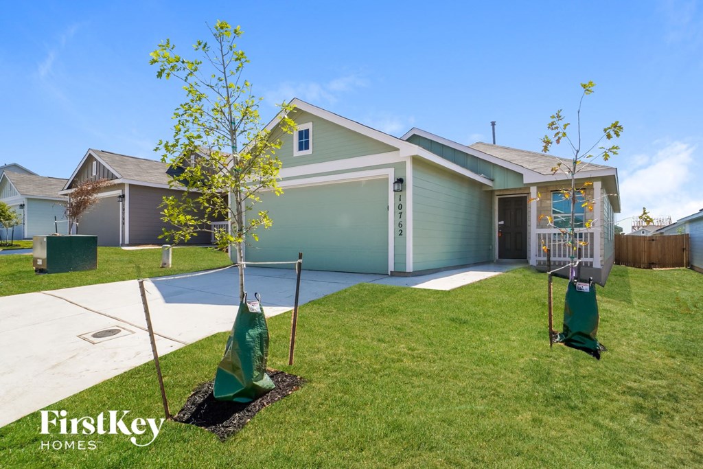 a home with two young trees in the front yard and a driveway