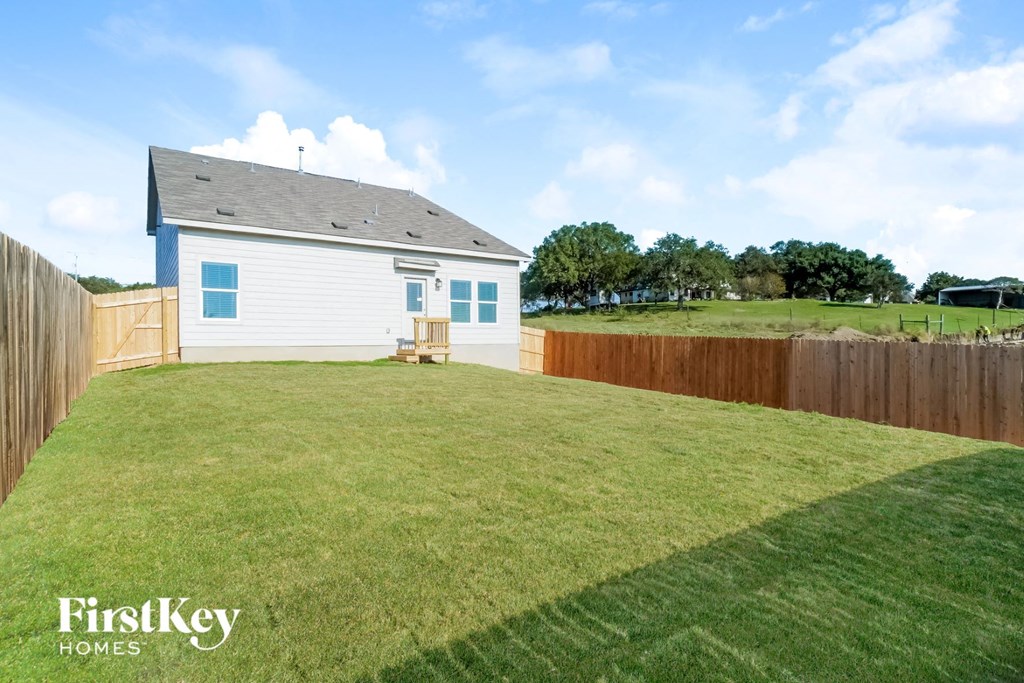 the backyard of a white house with a grassy yard and a fence