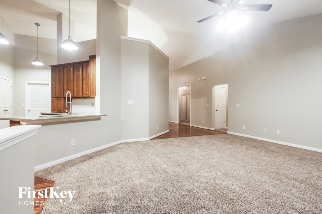 an empty living room with a kitchen and a ceiling fan