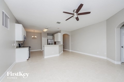 A spacious, empty room with a ceiling fan and a kitchenette.