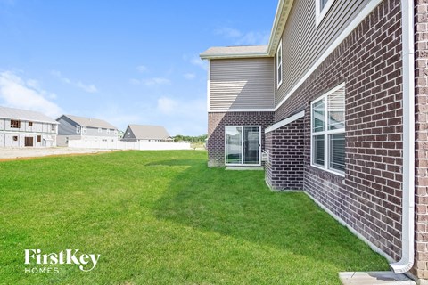 A brick house with a grassy lawn in front and a clear blue sky above.