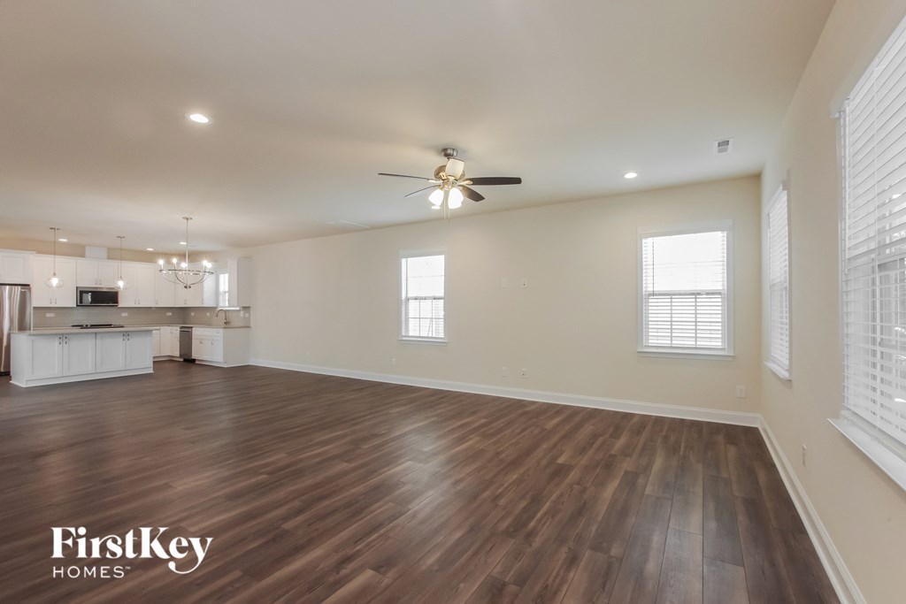 an empty living room with a ceiling fan and a kitchen
