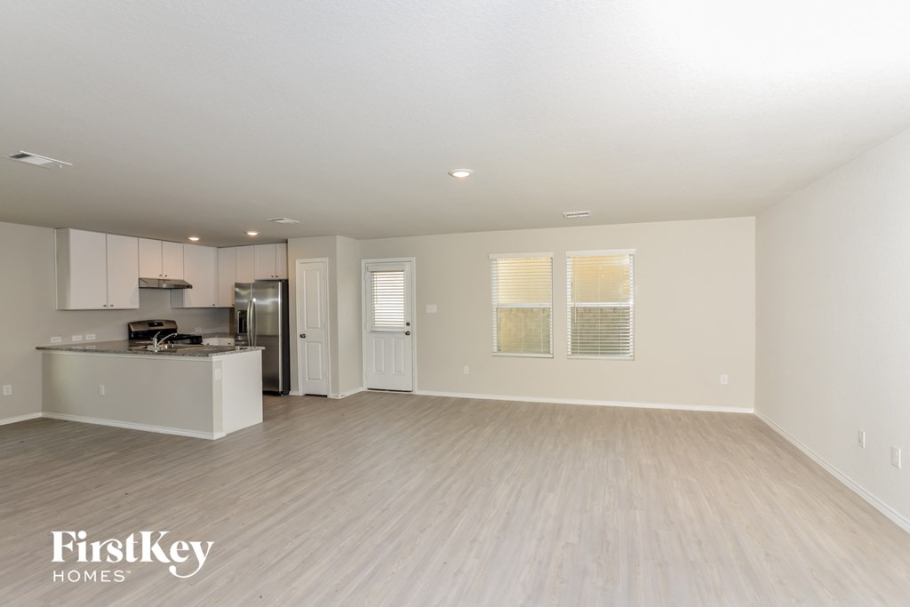 a spacious living room and kitchen with white walls and wood flooring