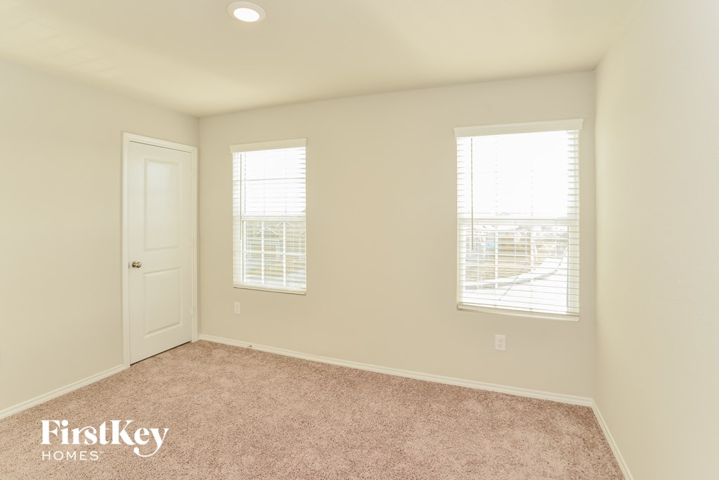 a bedroom with a carpeted floor and two windows and a door