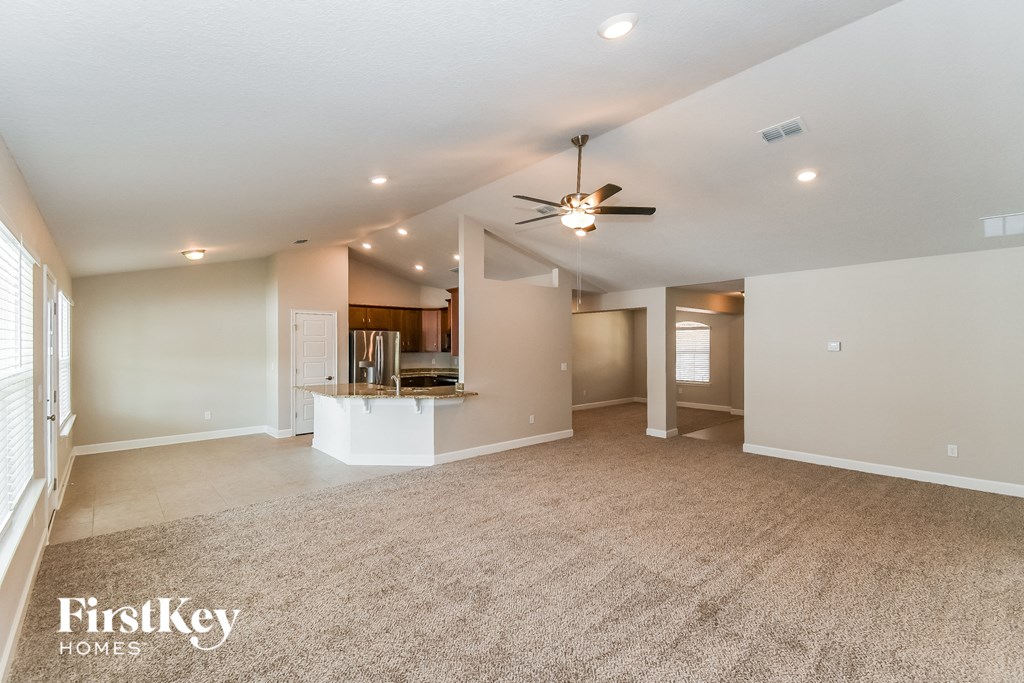 an empty living room with a ceiling fan and a kitchen