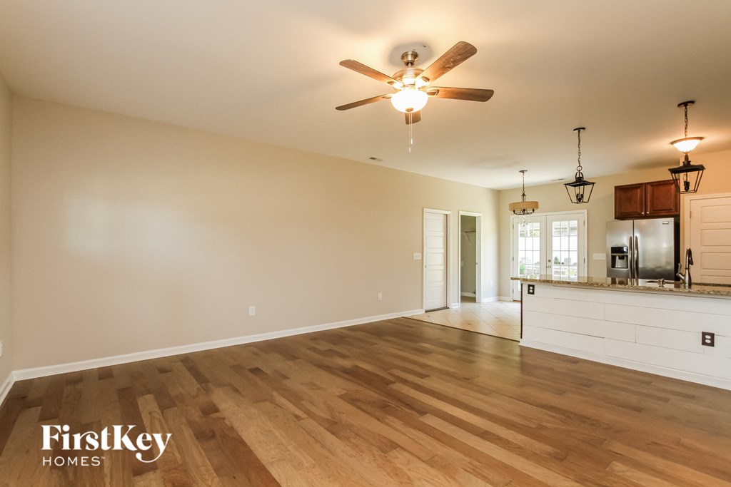 an empty living room with a ceiling fan and a kitchen