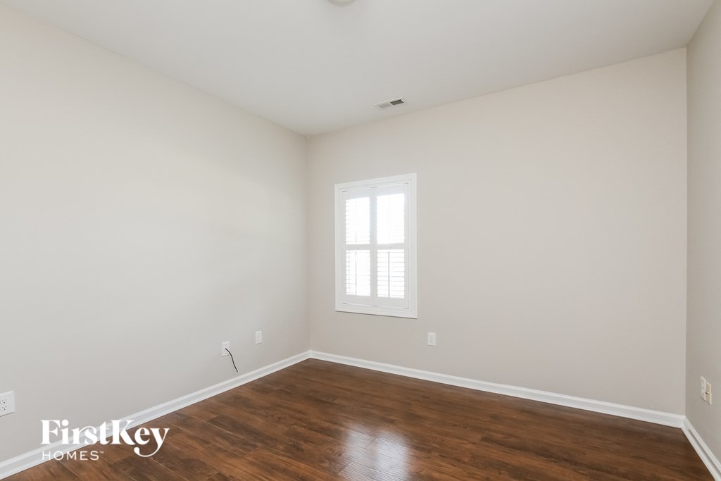 a bedroom with white walls and wood floors and a window