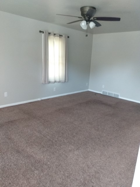 an empty living room with carpet and a ceiling fan