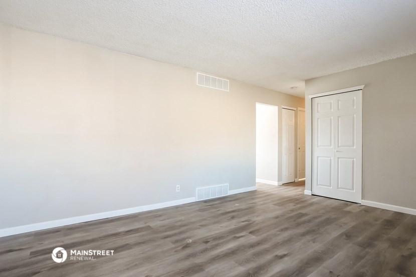 the spacious living room with white walls and wood flooring