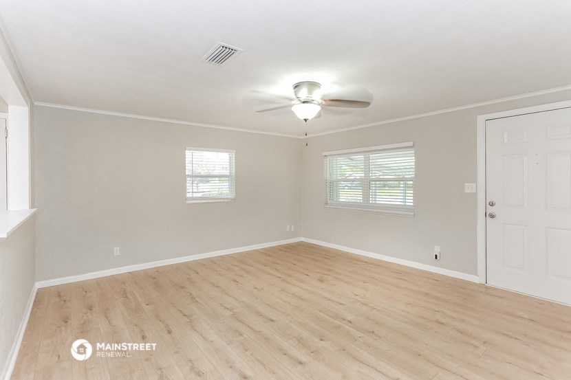 the spacious living room with wood flooring and a ceiling fan