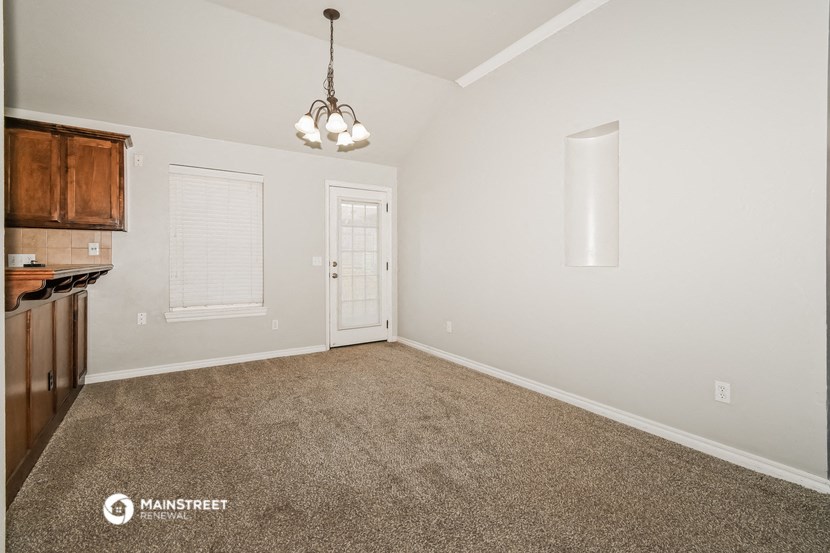 the spacious living room and kitchen with white walls and carpet