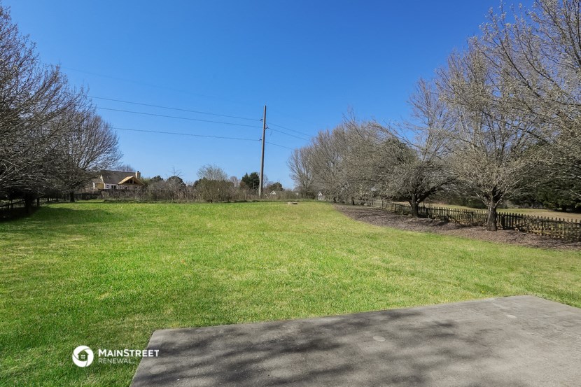 a large grassy field with trees and a driveway