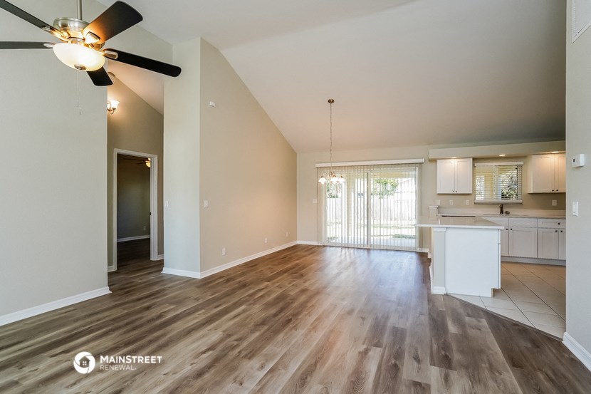 an empty living room with a ceiling fan and a kitchen