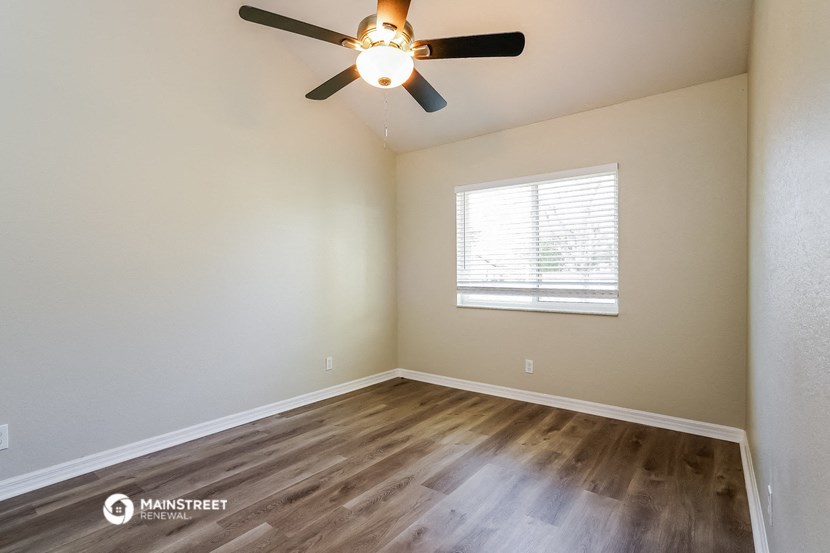 the spacious living room with wood flooring and a ceiling fan