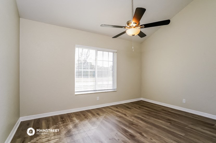 the spacious living room with a large window and a ceiling fan