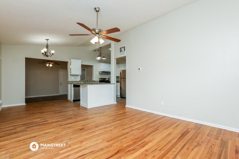 an empty living room with a ceiling fan and a kitchen
