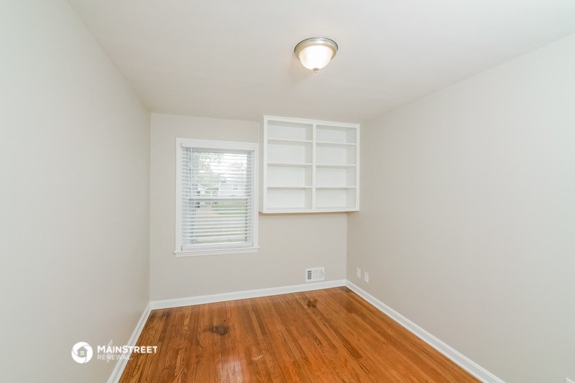 a bedroom with a hardwood floor and a window with white shelves