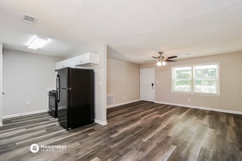 an empty living room with a refrigerator and a ceiling fan