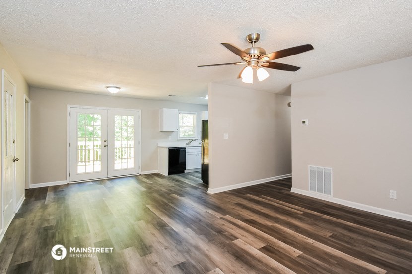 an empty living room with a ceiling fan and a kitchen