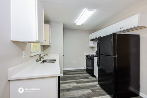 a kitchen with white cabinets and a black refrigerator and a sink