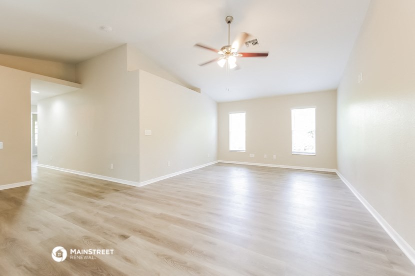 the spacious living room with hardwood floors and a ceiling fan