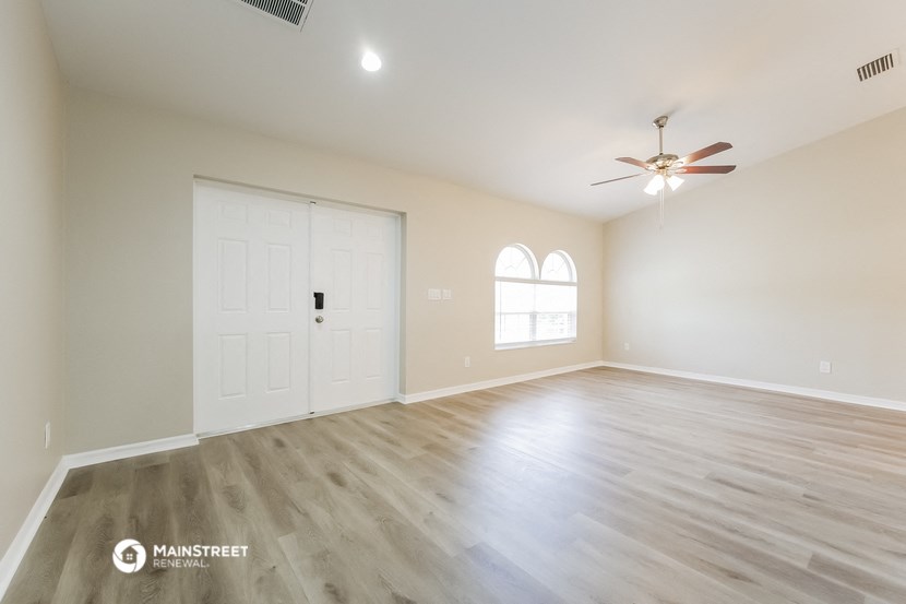 the spacious living room with hardwood floors and a ceiling fan