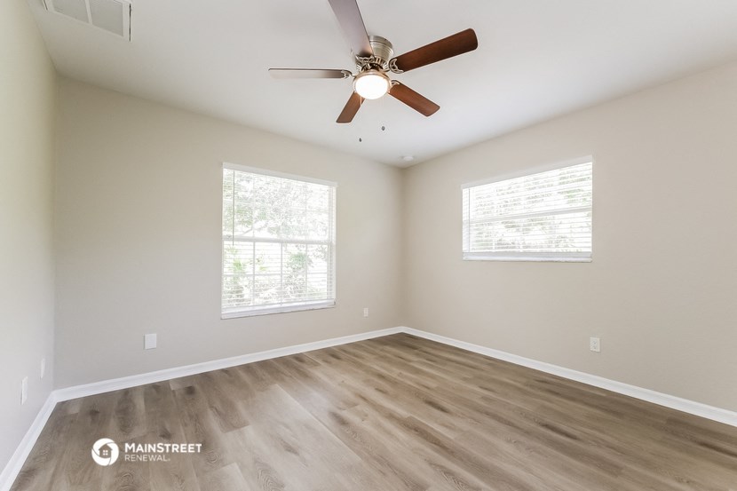 an empty room with a ceiling fan and two windows