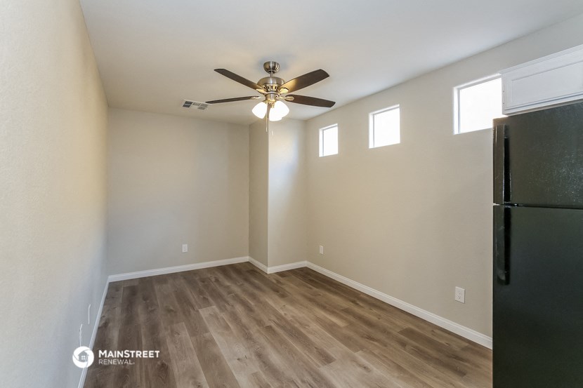 an empty living room with a refrigerator and a ceiling fan