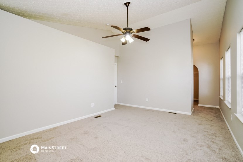 the spacious living room with ceiling fan and white walls