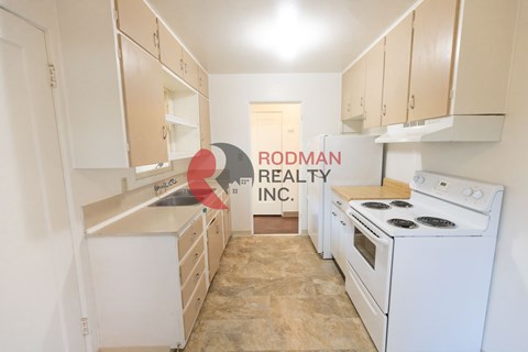 A kitchen with white appliances and cabinets is shown with a sign that says Rodman Realty Inc.