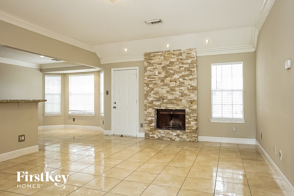 an empty living room with a stone fireplace in the center