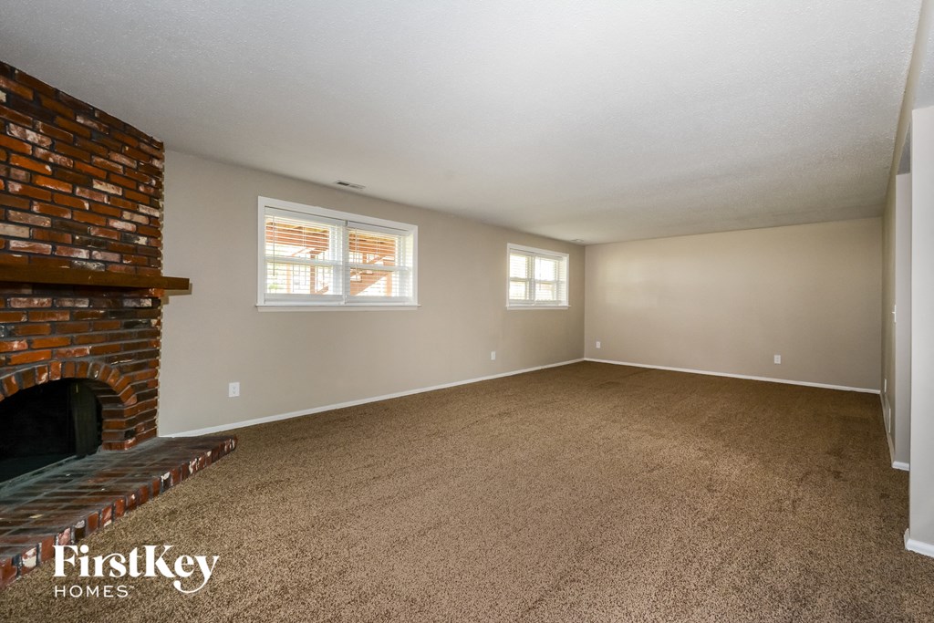 A room with a brick fireplace and two windows.