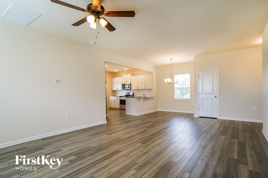 an empty living room with a ceiling fan and a kitchen