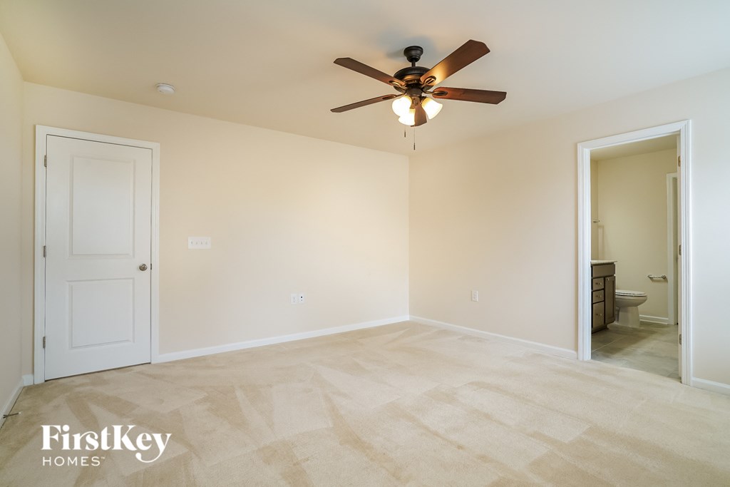 a empty living room with a ceiling fan and a door to a bathroom