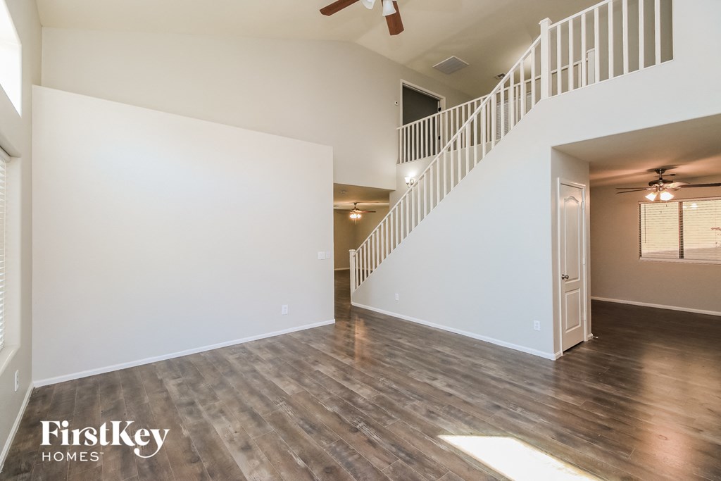 A spacious room with wooden flooring and a staircase leading to another room.