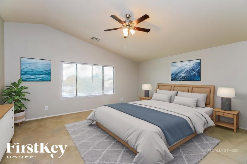 A bedroom with a large bed, a ceiling fan, and two pictures on the wall.