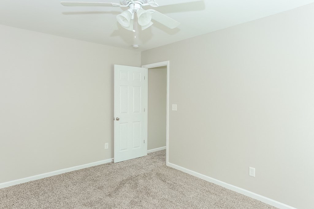 an empty bedroom with a ceiling fan and a door to a closet