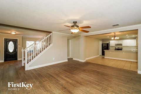 A spacious living room with a staircase and a ceiling fan.