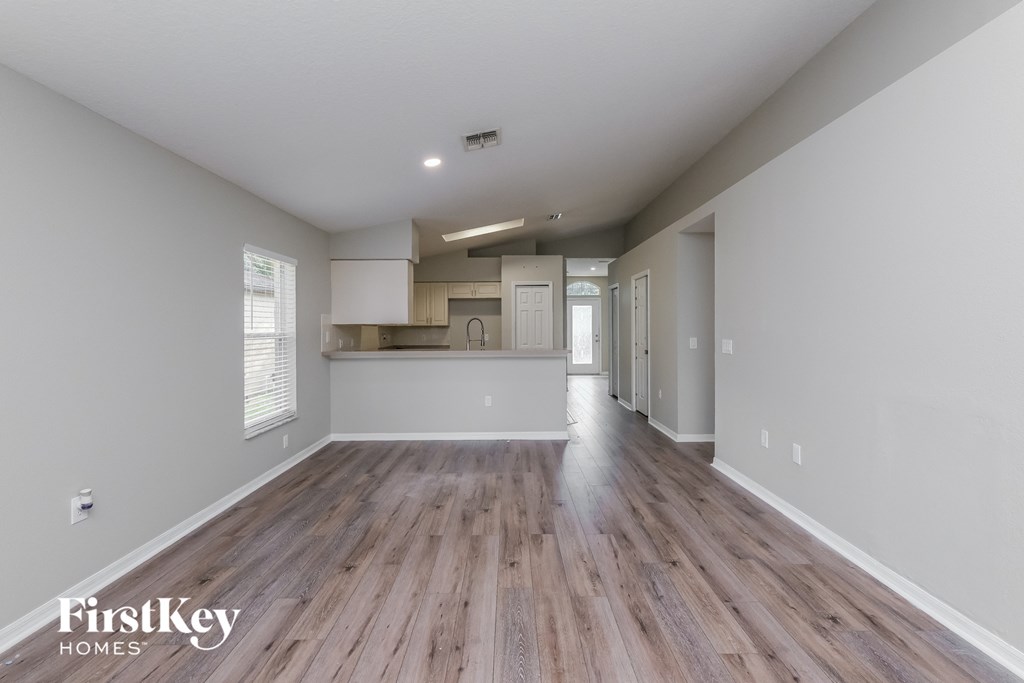 A spacious room with wooden flooring and a kitchen area in the background.
