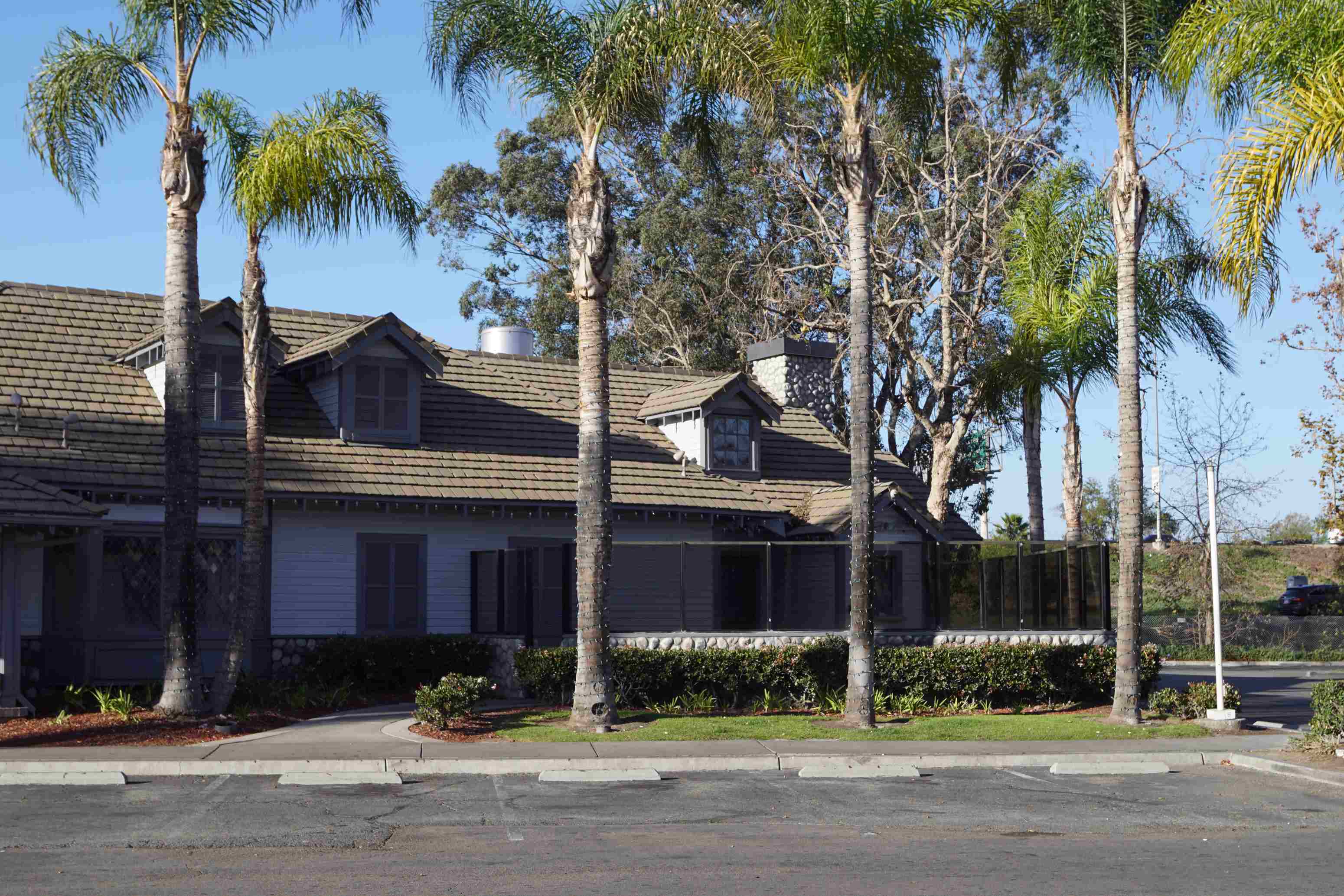 A building with a brown roof and white walls is surrounded by palm trees.
