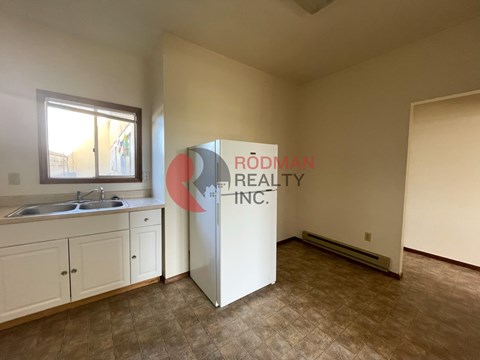 A kitchen area with a sink, cabinets, and a refrigerator.