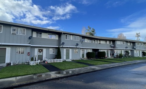 A row of grey houses with white fences in front.
