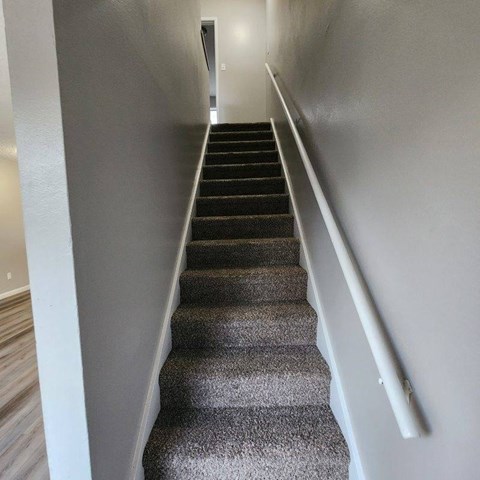 A staircase with a grey carpeted runner and white handrails.