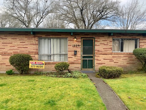 A red brick house with a sign that says "For Rent" and a phone number.