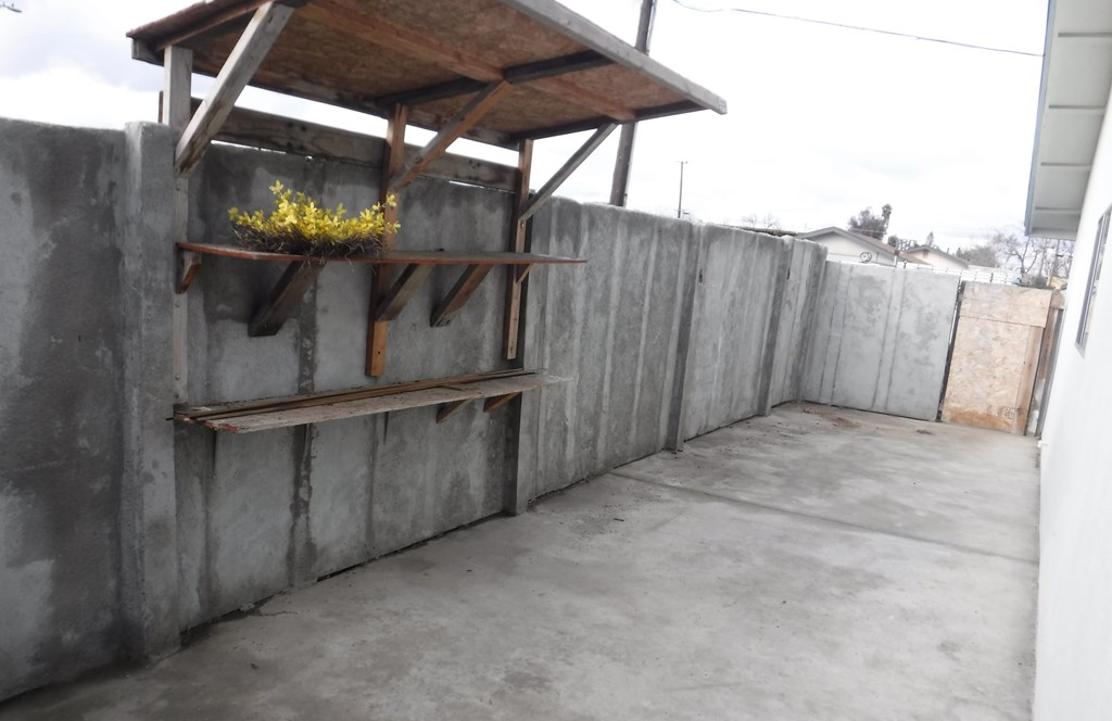 a patio with a wooden fence and a shelf with a plant on it