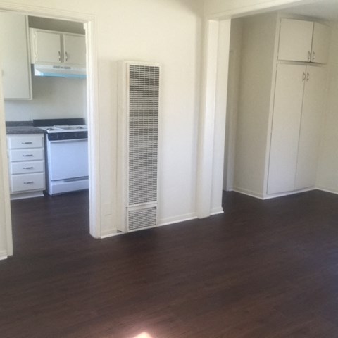 an empty living room with a hard wood floor and a heater in the corner