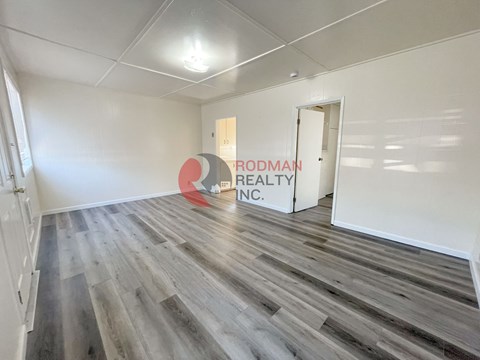 A room with wooden flooring and a sign that says "Rodman Realty Inc.".
